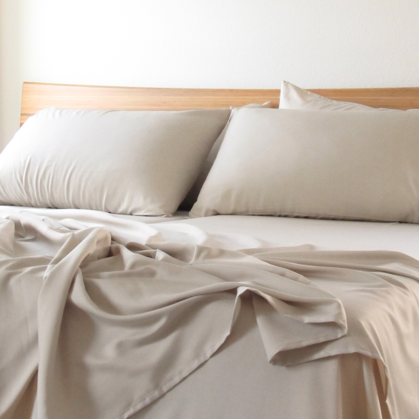 Taupe Copper Infused Bamboo Pillowcase Set on a bed with a wooden headboard.